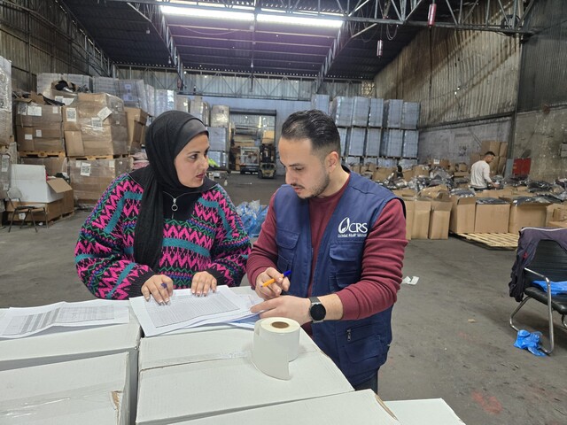 © CRS Staff Zwei Caritas-Mitarbeitende prüfen Listen in einer Lagerhalle mit Hilfsgütern.