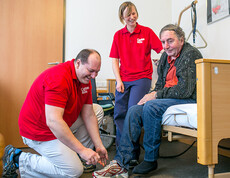 Zwei BetreuerInnen der Caritas Altenpension helfen einem Mann beim Schuhe anziehen.