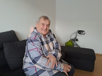 Ein älterer Mann mit Rollator sitzt auf einem Sofa