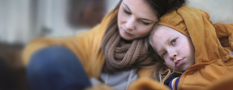 Ukrainian immigrants mother with daughter with luggage waiting at train station wrapped in blanket