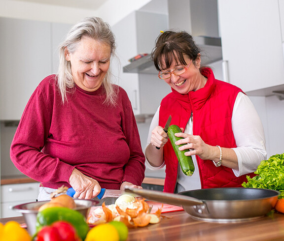 Eine alte Frau und eine Betreuerin beim Kochen in der Caritas Altenpension.