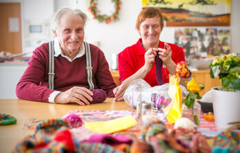 Ein alter Mann und eine ältere Frau sitzen am Tisch und stricken. 